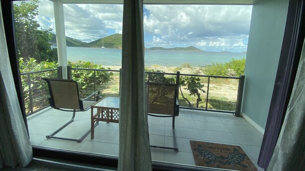 A balcony with two chairs and a table, overlooking a beach and the sea. - Oceanfront Beach Luxury Retreat (St Thomas)