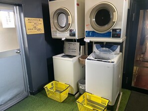 Zona de bugaderia amb dues rentadores, un assecador i dues cistelles grogues.