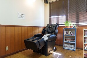 Een massagestoel in een kamer met houten lambrisering, een boekenkast vol tijdschriften en een bord aan de muur.