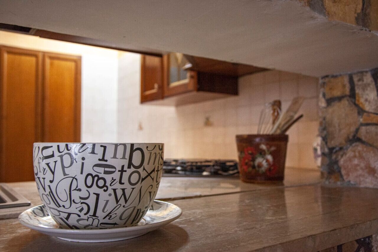 Een keuken met een beker op het aanrecht, houten kastjes en een stenen muur.