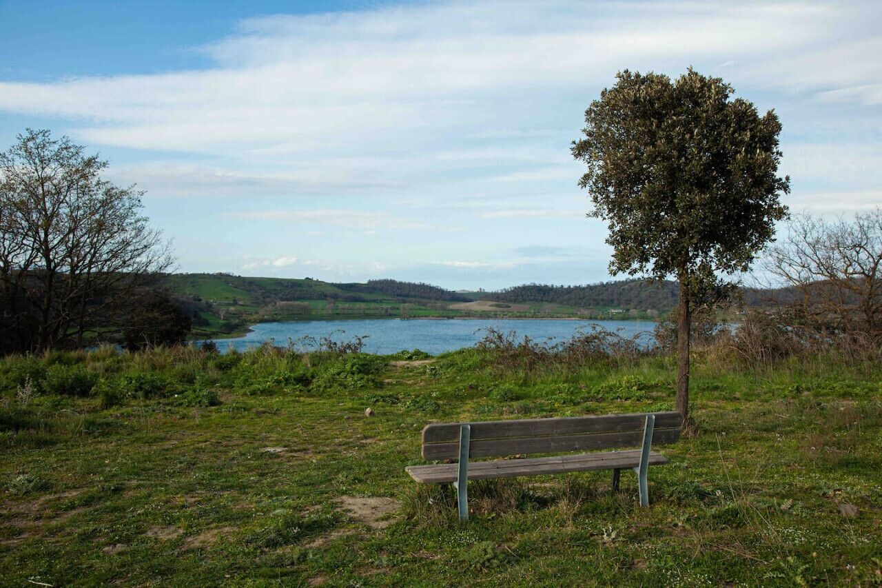 A bench in a grassy area with a lake and hills in the background.
