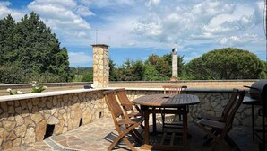 Une terrasse extérieure avec des murs en pierre, une cheminée en pierre et des meubles en bois.
