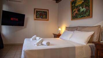 A hotel room with a bed, a TV displaying 'NETFLIX', a painting, and a lamp.