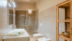 Ein modernes Badezimmer mit einer Duschkabine, einem weißen Waschbecken, einer Toilette und einem Bidet.