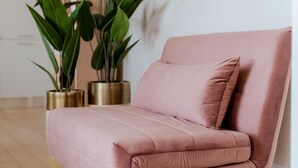 Ein rosafarbenes Sofa mit Kissen, zwei Topfpflanzen und ein Holzboden.