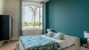 Ein Schlafzimmer mit Bett, einem fensterbelaubten Fenster, Blick auf Bäume und einer dunkel gefärbten Wand.