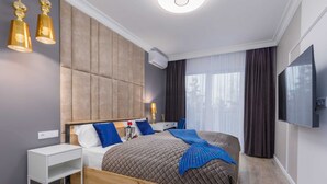 A modern hotel room with a large bed, a bedside table, a TV, and a window with curtains.
