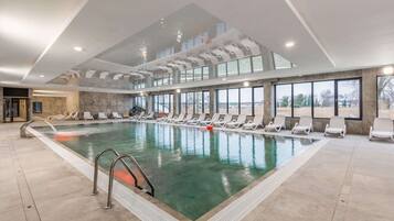 A large indoor swimming pool with clear water, surrounded by lounge chairs and a modern ceiling design.