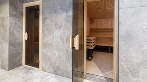 A sauna with a wooden interior and a glass door, set against a grey tiled wall.