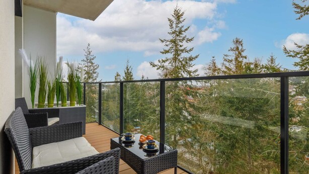 A balcony with wicker furniture, a table with cups and pastries, and a view of trees and buildings. - Stylish Apartment | Wellness, Parking (Dziwnów)