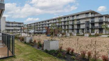 A modern multi-story building with balconies, a parking area, and landscaped garden beds.