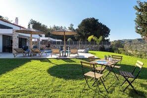 A modern outdoor patio with a pool, lounge chairs, and umbrellas. - Aiora Luxury Villas - Villa 2 (Afantou)