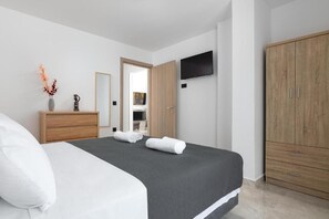 A hotel room with a bed, a wooden wardrobe, a flat-screen TV mounted on the wall, and a mirror. - Aiora Luxury Villas - Villa 2 (Afantou)