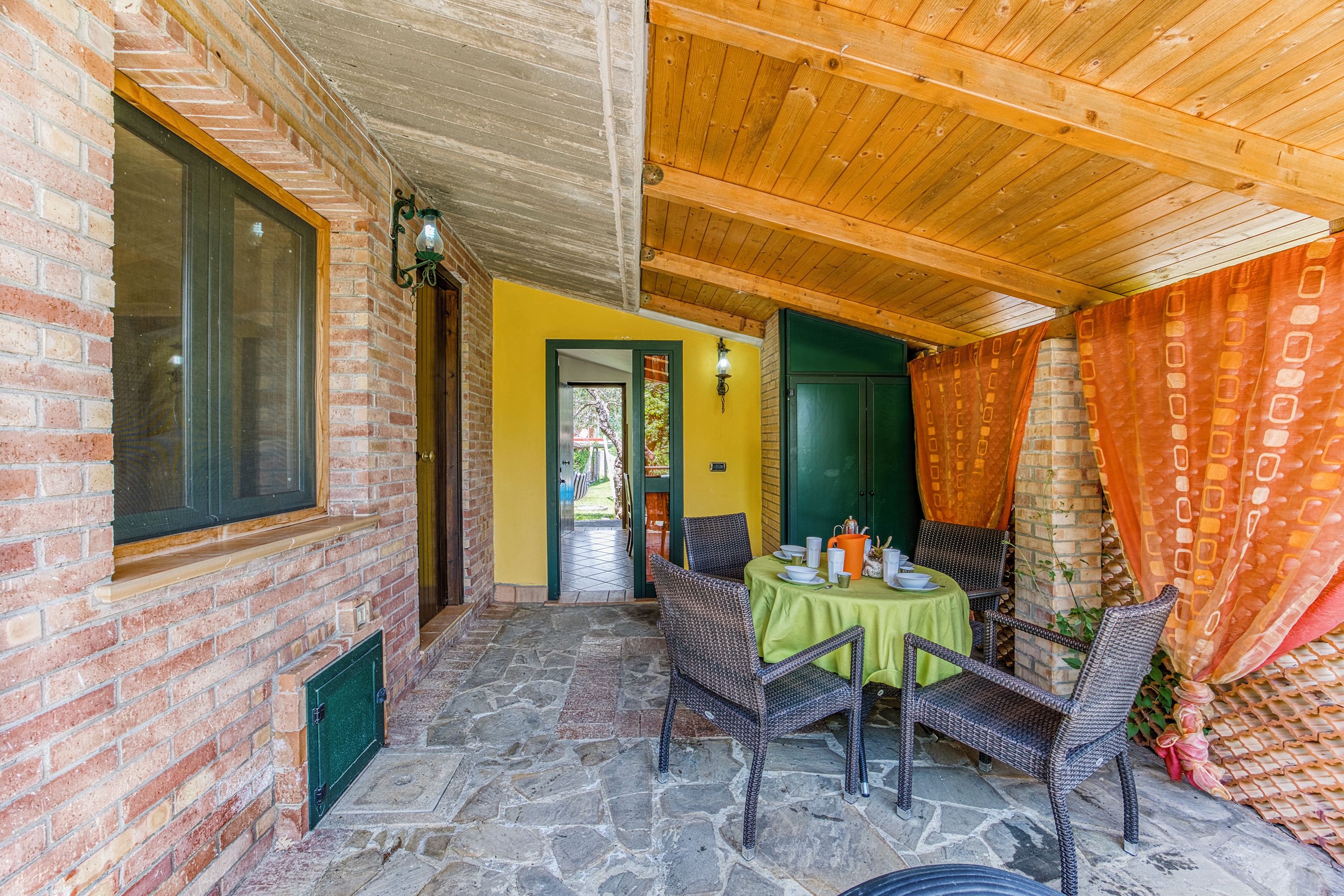 A covered patio with stone flooring, wicker furniture, and a green tablecloth.