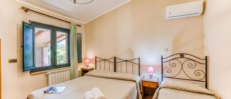 A bedroom with two beds, a chandelier, an air conditioner, and a window with curtains.
