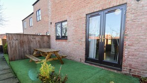 Une terrasse avec une table et des bancs en bois, entourée d’un mur de briques et d’une porte en verre.