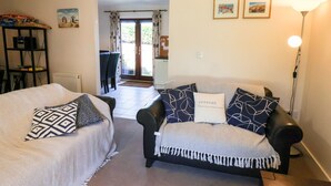 Un salon avec deux canapés, une table basse et une lampe. Une porte donne accès à un balcon.