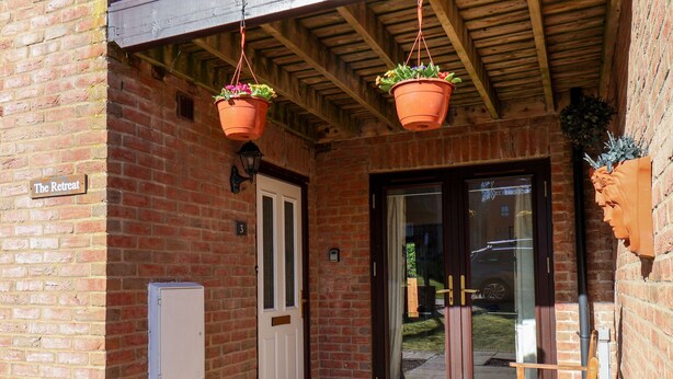 Un bâtiment en briques avec une porte en bois, une enseigne indiquant «The Retreat» et des pots de fleurs suspendus.