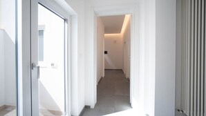 Un couloir avec une porte vitrée, un radiateur et un sol carrelé.