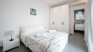 Une chambre d’hôtel moderne comprenant un lit, une table de chevet, une salle de bain avec un miroir et un lavabo, ainsi qu’une grande armoire.