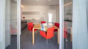 Un espace repas moderne avec une table en bois, des chaises rouges, un canapé et une cuisine en arrière-plan.