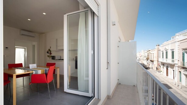 Un balcon doté d’un espace repas, d’une porte-fenêtre coulissante et offrant une vue sur une rangée d’immeubles.
