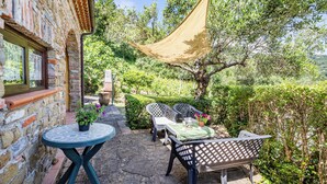 A patio with a table and chairs, a hanging shade, and a view of the surrounding greenery.