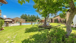 A backyard with a swimming pool, a swing set, and a tree.