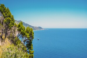 A coastal landscape with a clear view of the sea, a boat, and distant mountains.