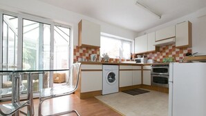 Une cuisine moderne avec une table en verre, un lave-linge, un four et une vue à travers la porte vitrée.