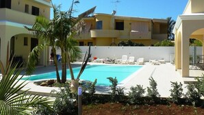 A pool area with lounge chairs, palm trees, and a clear blue sky.