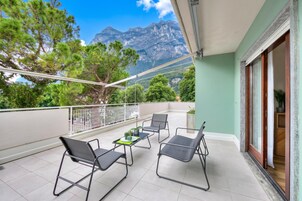 A balcony with chairs and a table, a view of mountains, and a door leading to a room.