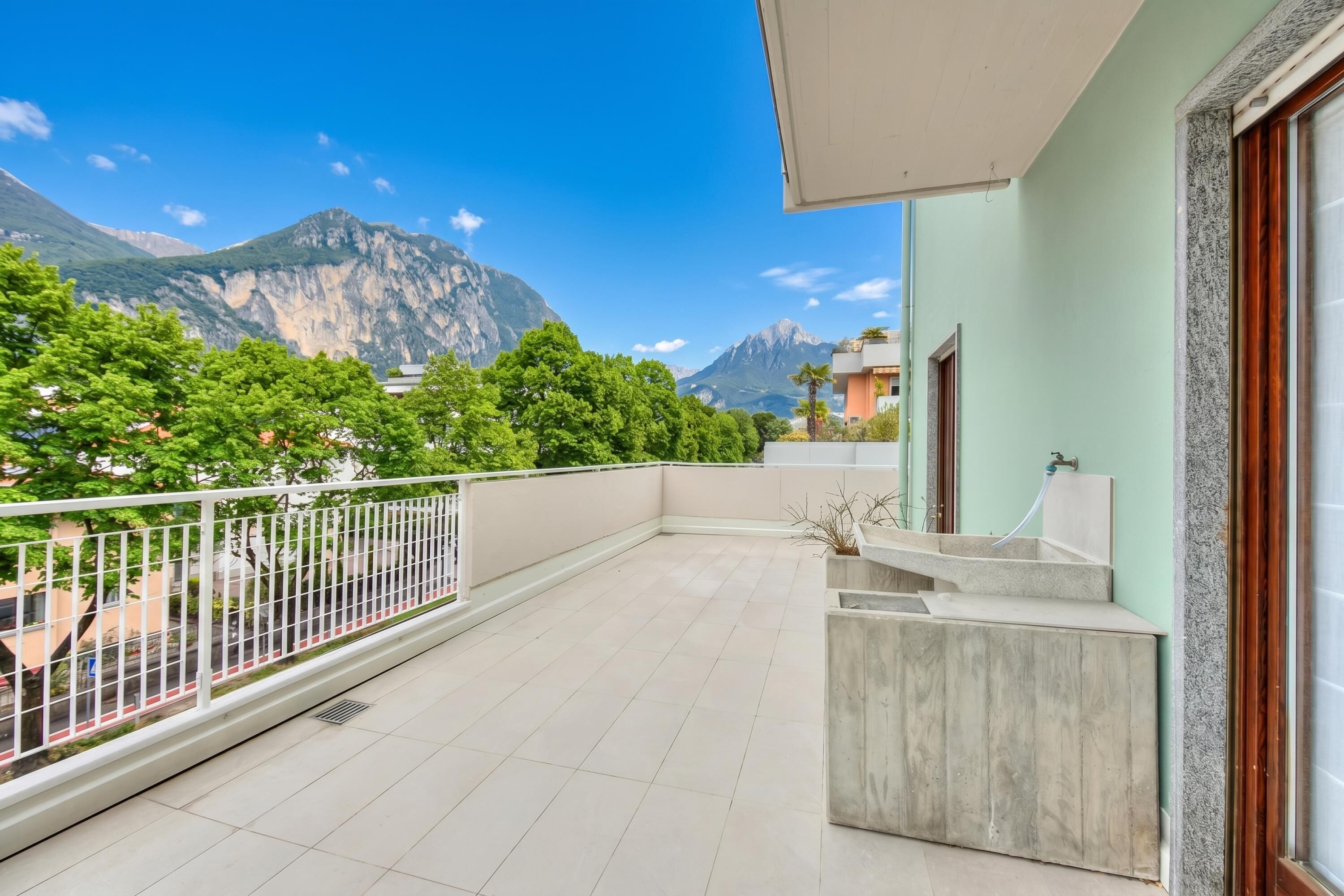 Uma varanda com vista para montanhas, corrimão branco e um vaso de concreto.