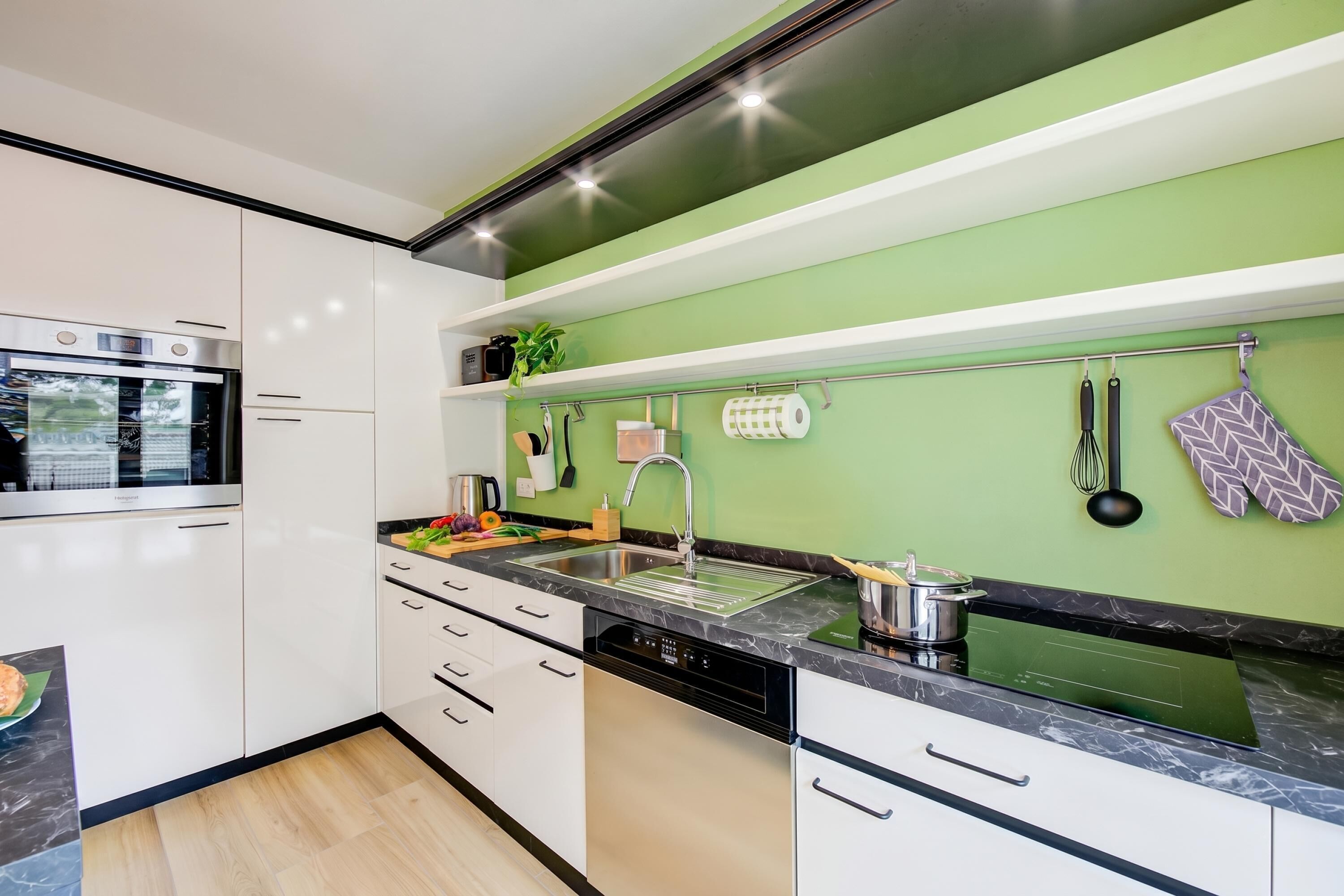 Una cocina moderna con armarios blancos, una encimera negra y una pared de acento verde.