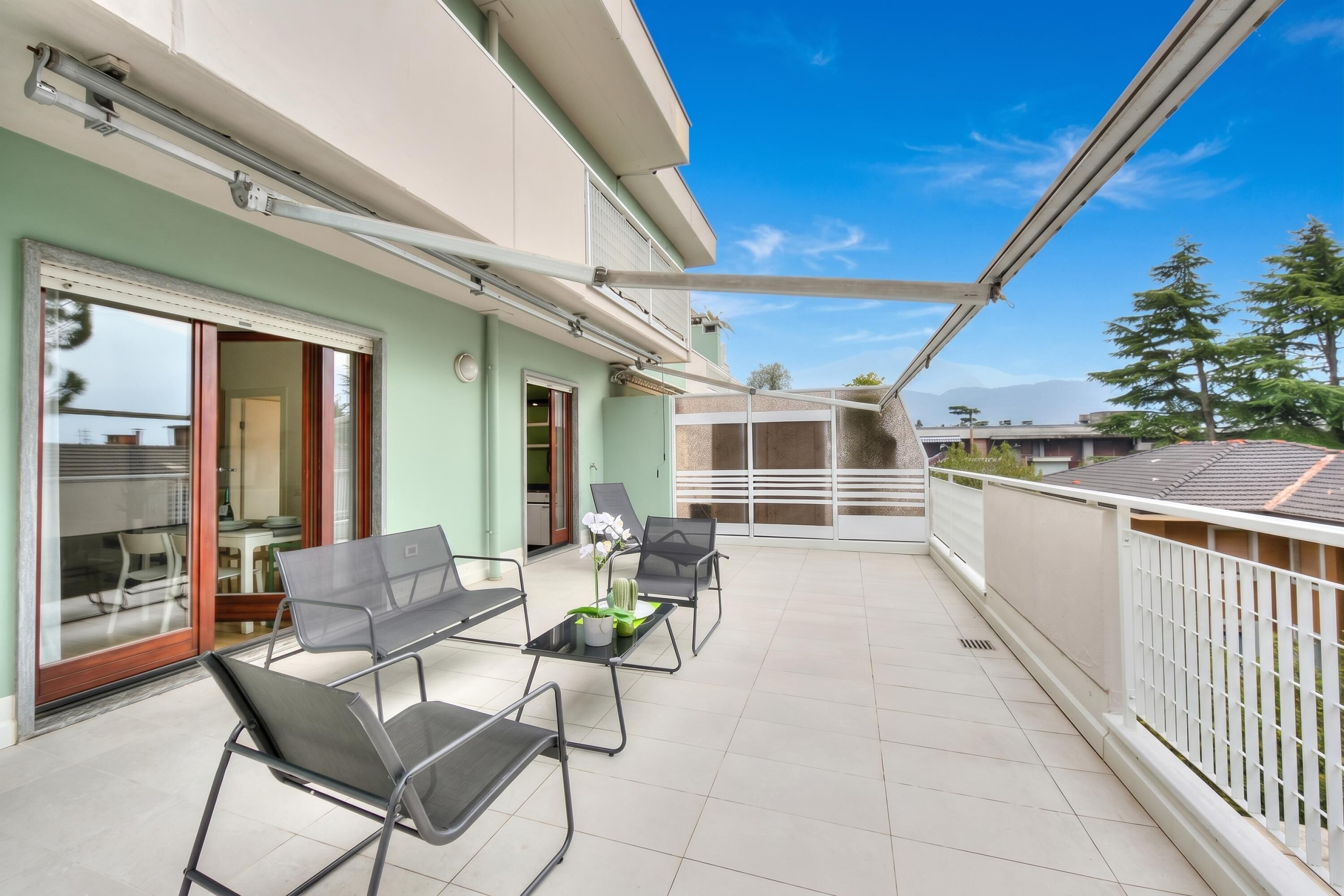 Ein Balkon mit Stühlen und Tisch, eine Schiebeglastür und Blick auf die Umgebung.