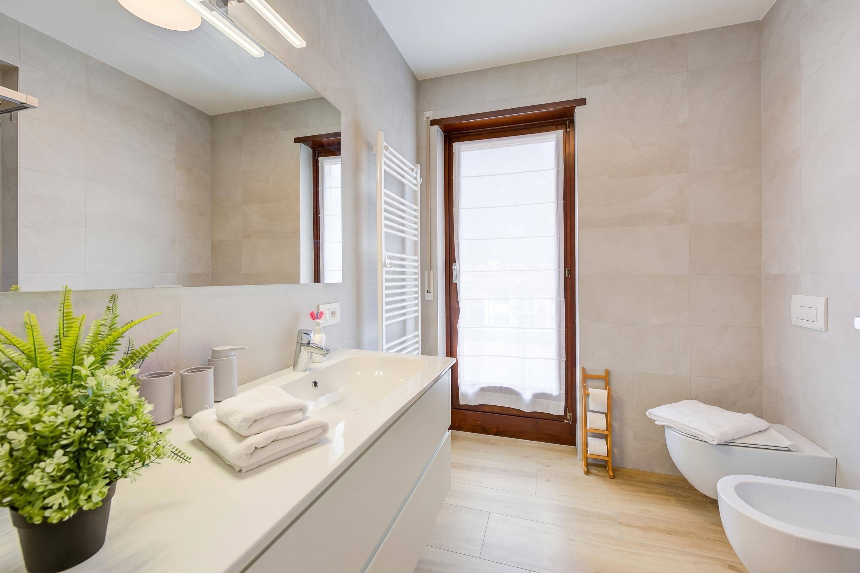 A modern bathroom with a large mirror, a white sink, a toilet, and a shower area.