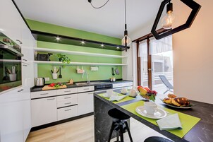 A modern kitchen with white cabinets, a green accent wall, and a dining area with a black countertop.