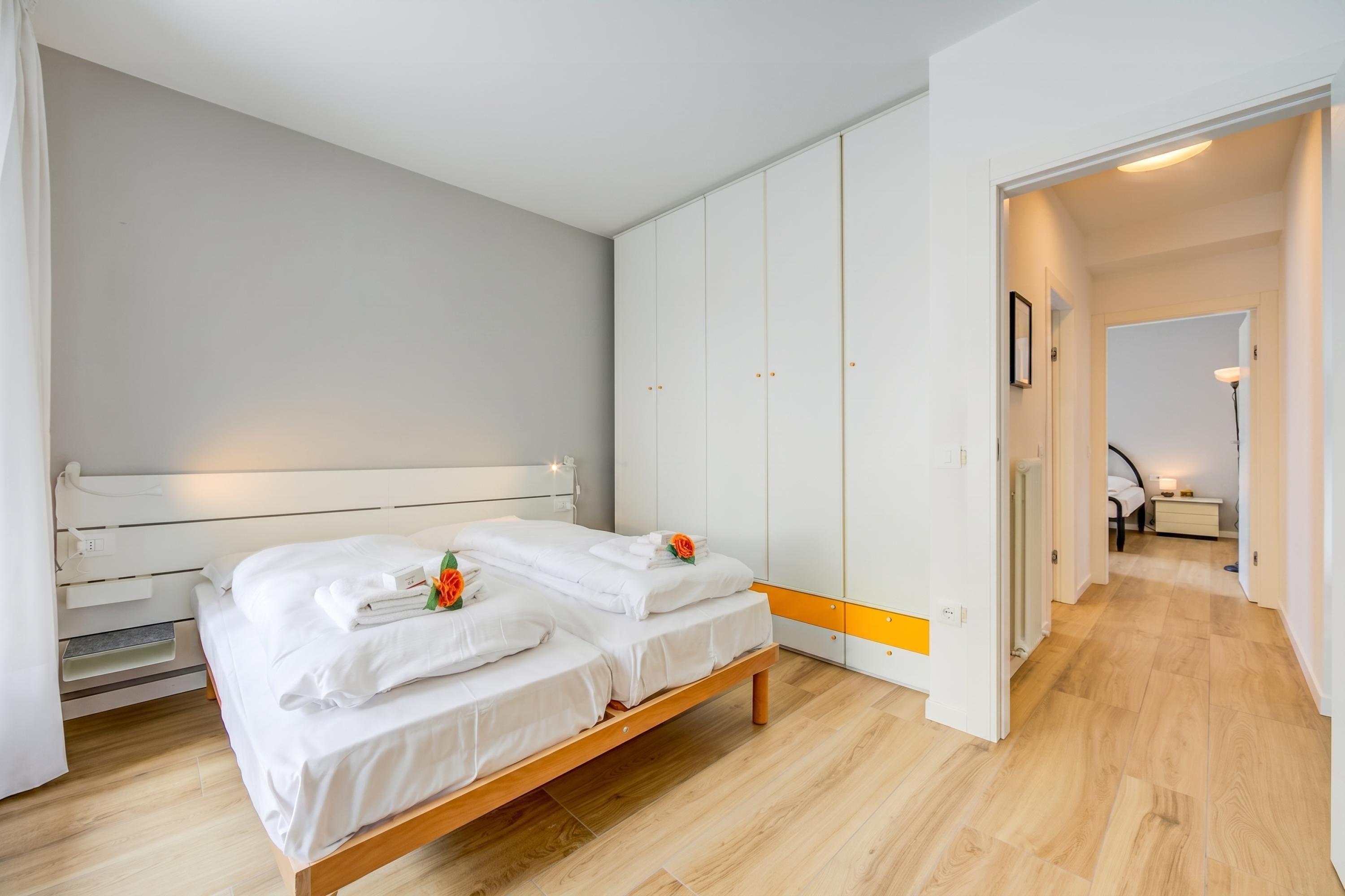 A bedroom with a bed, white wardrobe, wooden flooring, and a hallway leading to another room.