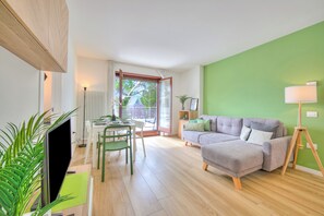 A modern living room with a grey sofa, a dining table with chairs, a TV, and a green wall. - Balcone Sui Tigli Few Min From The Lake (Riva del Garda)