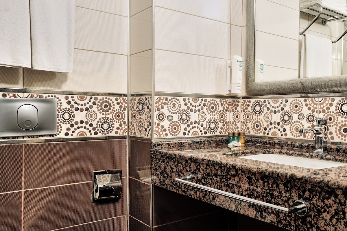 Casa de banho com azulejos estampados, lavatório, dispensador de toalhas e zona de duche.