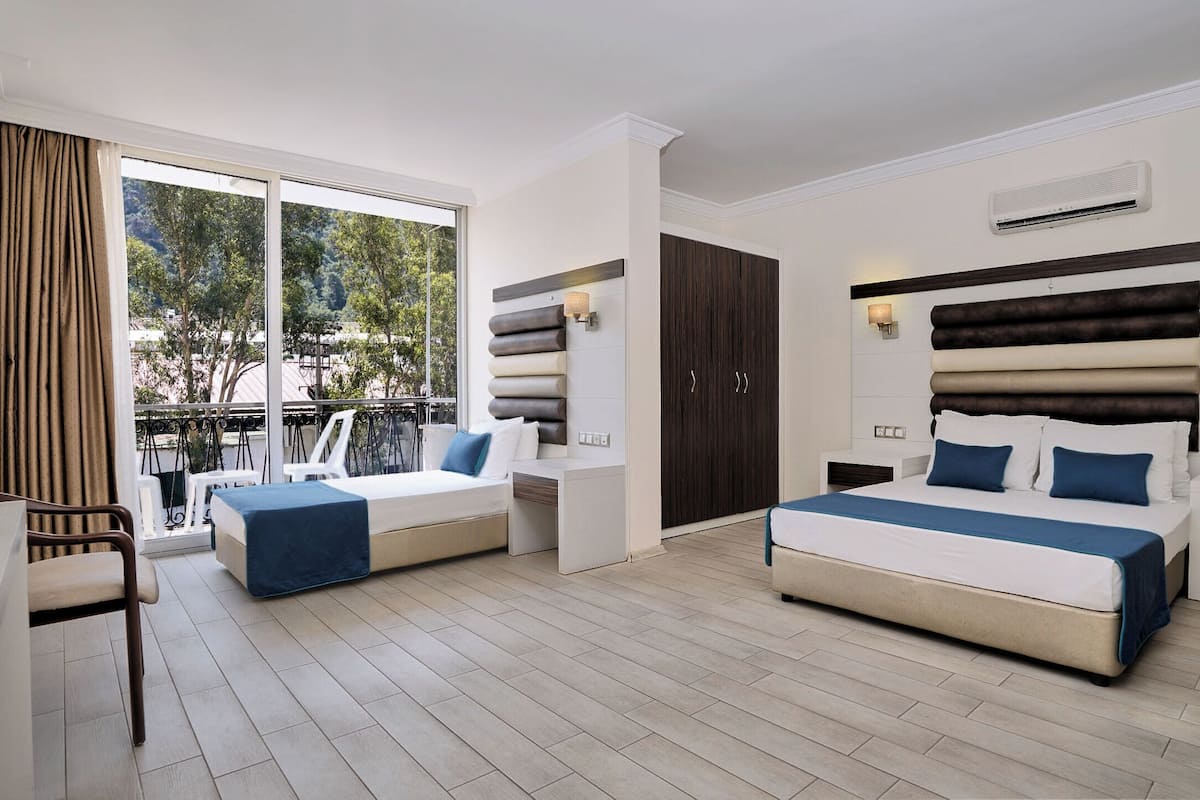 A modern hotel room with two beds, a balcony, and a view of greenery.