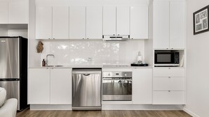 A modern kitchen with white cabinetry, stainless steel appliances, and a wooden floor. - Edge One - Dog Friendly (Jindabyne)