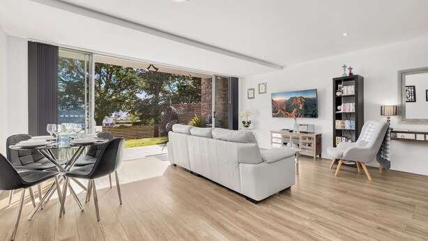 A modern living room with a white sofa, a dining table with chairs, a TV, and a bookshelf. - Edge One - Dog Friendly (Jindabyne)