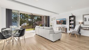 Una sala moderna con un sofá blanco, una mesa de comedor con sillas, un televisor y una estantería.