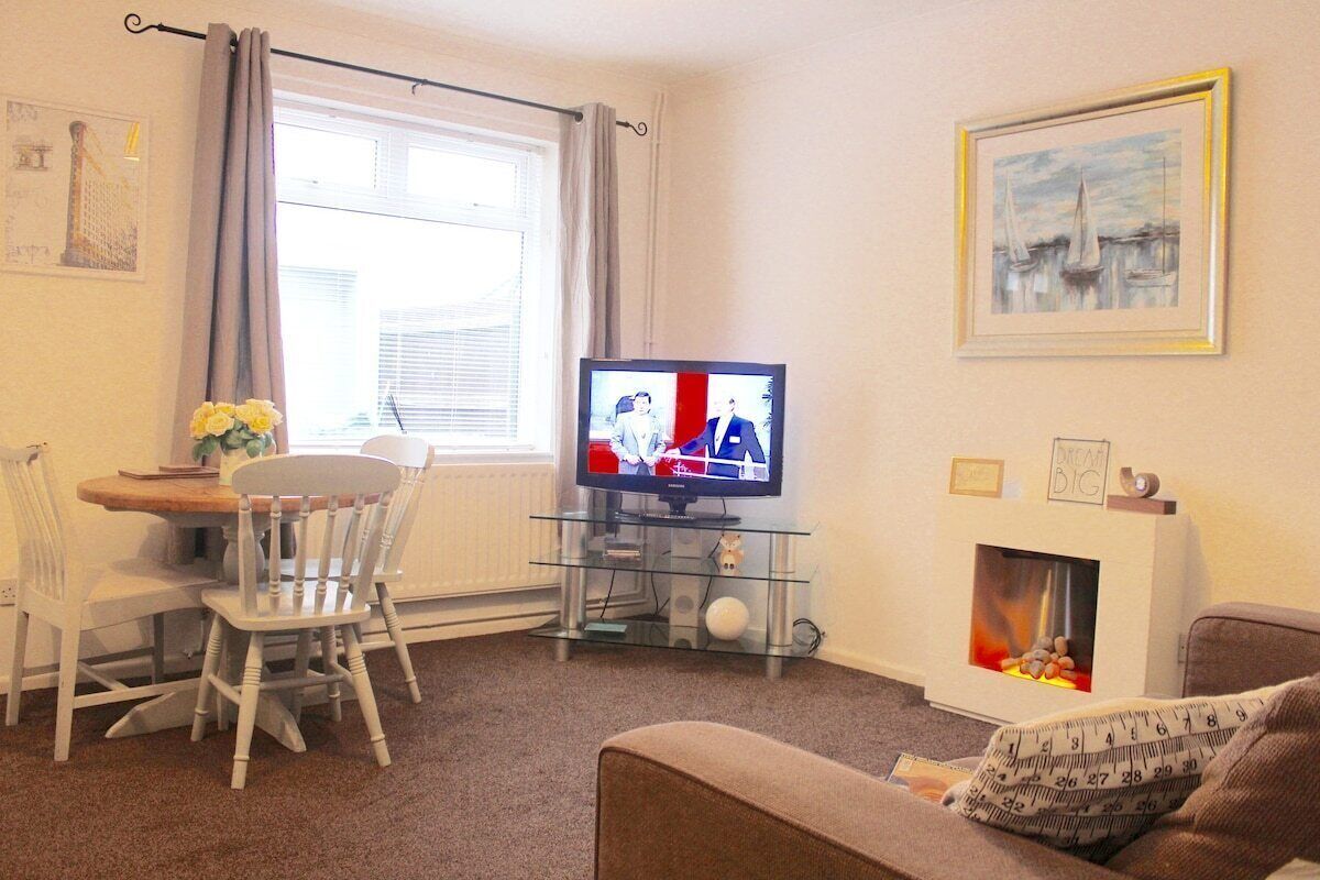 A living room with a TV, a fireplace, a dining table with chairs, and a painting on the wall.