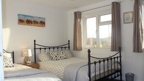 Ein Schlafzimmer mit zwei Betten, einem fensterbelaubten Fenster, einem Bild an der Wand und einem Nachttisch mit Lampe.