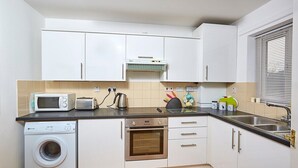 Eine kleine Küche mit Waschmaschine, Mikrowelle, Toaster, Backofen und einem Fenster mit Jalousien.