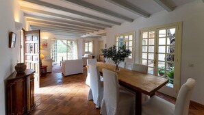 A spacious dining area with a wooden table and white chairs, large windows with shutters, and a rustic ceiling with exposed beams. - Casa Perdita, ideal for family and relaxed vacations (Deiá)