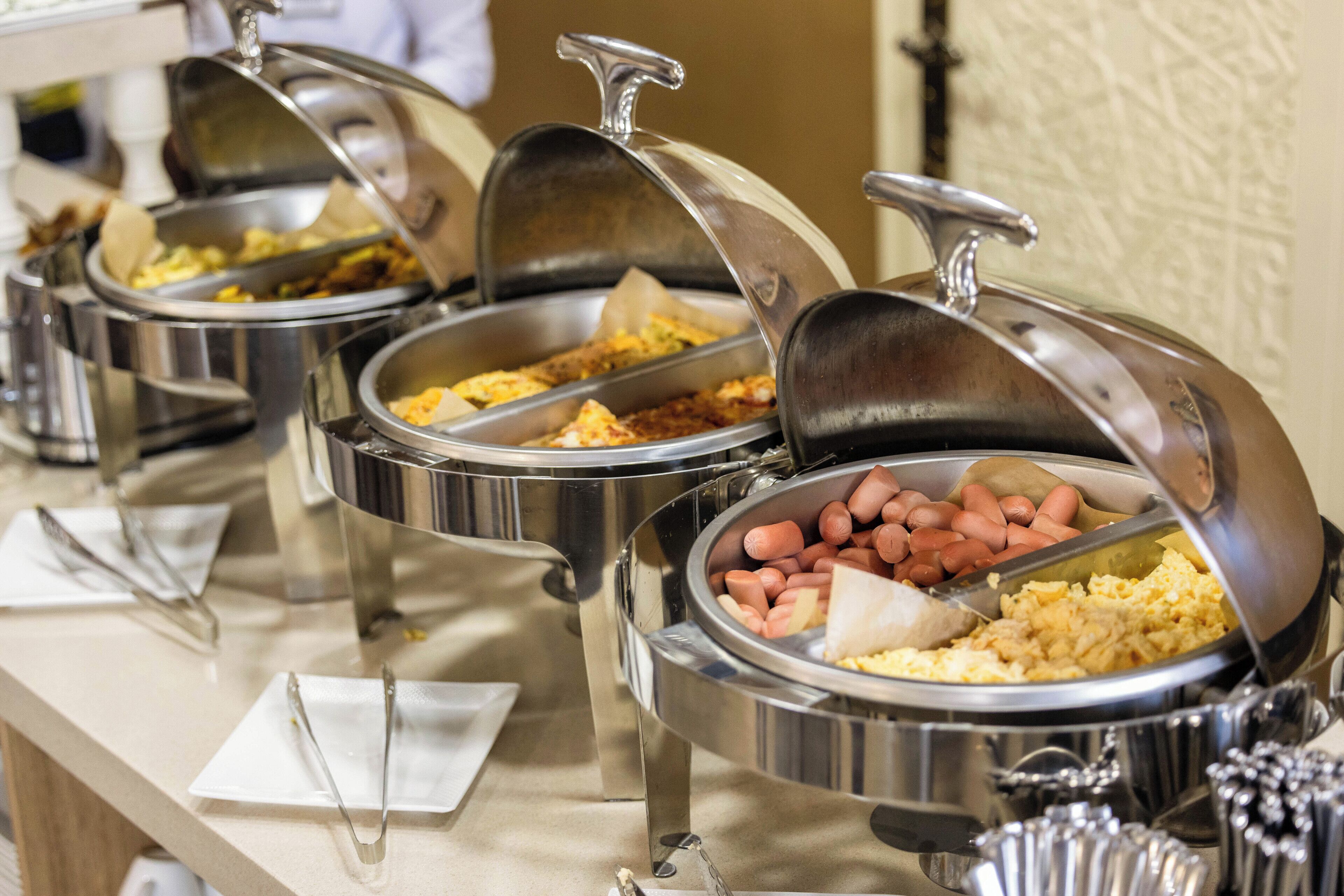 A buffet with multiple stainless steel chafing dishes containing various foods.
