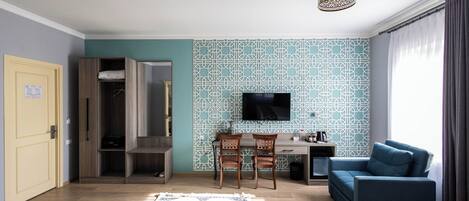 A modern living room with a blue sofa, a TV mounted on the wall, and a wooden desk with chairs.